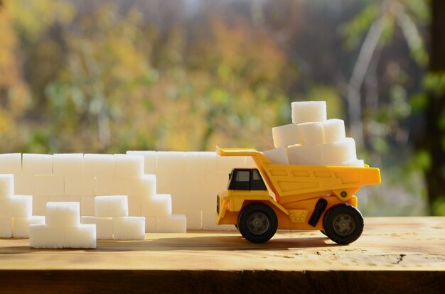 A small yellow toy truck is loaded with white sugar cubes near the sugar wall. 