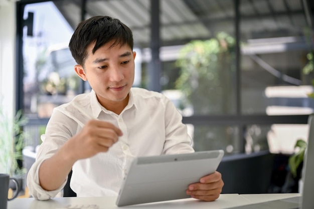 Uomo d'affari asiatico intelligente che pianifica un progetto utilizzando il suo tablet e lavorando in ufficio