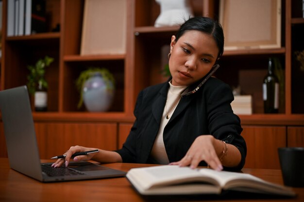 Smart Asian female boss on the phone call with her assistant while working on her tasks