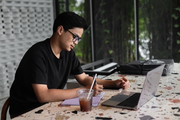 Smart Asian male college student studying using a laptop at the cafe or coffee shop