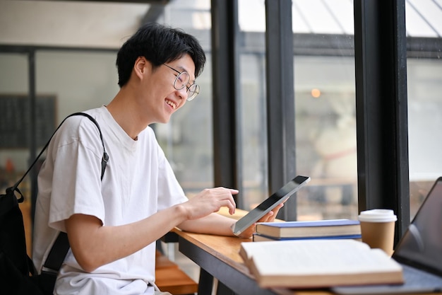 Smart Asian male college student using his tablet anda working on school project at a cafe