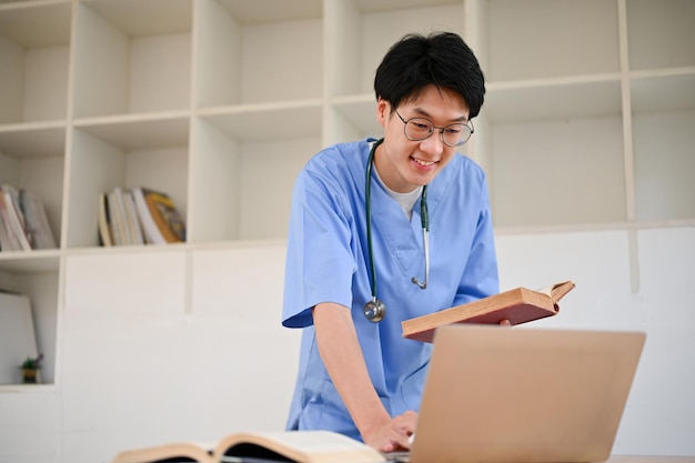 Smart Asian male medical student using laptop researching medical paper on internet