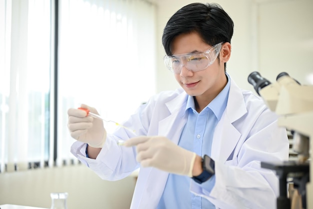 Smart Asian male scientist concentrating adjusts a virus sample in a Petri dish in his lab