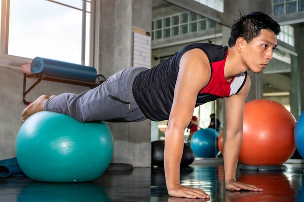 Smart Asian man in sportswear training abdominal muscles with ball gym at fitness.