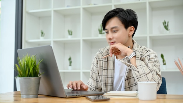 Smart Asian man using laptop computer working on his project assignment in the office