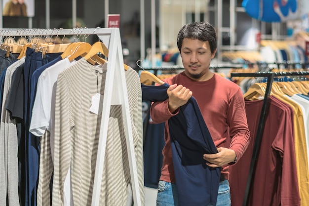 ショッピングセンターで衣料品店で服を選んだ髭を持つスマートなアジア人男性