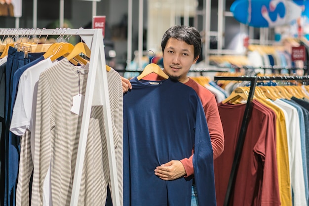 쇼핑 센터에서 옷 가게에서 옷을 선택하는 수염을 가진 똑똑한 아시아 사람