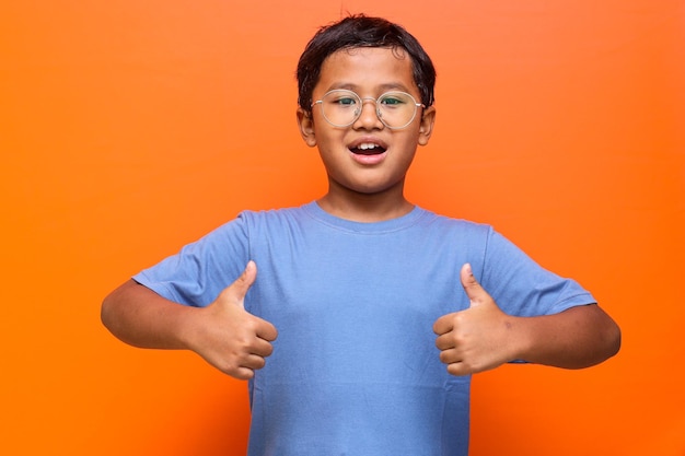 Smart Asian schoolboy showing thumb up against orange background