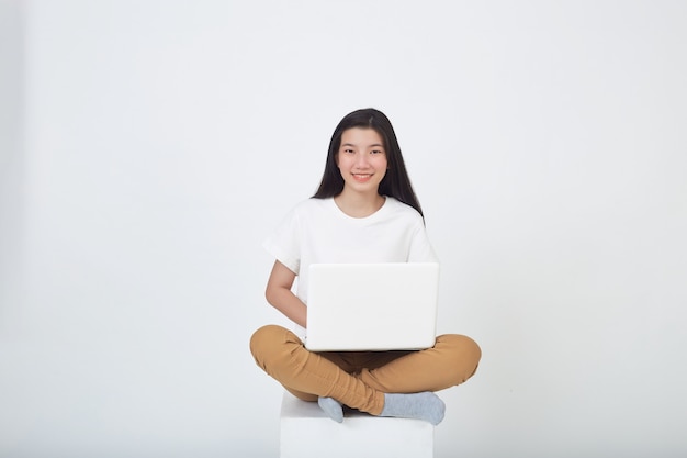 똑똑한 매력적인 젊은 여성은 회색 스튜디오 배경에 다리를 꼬고 앉아 노트북 컴퓨터를 사용합니다.