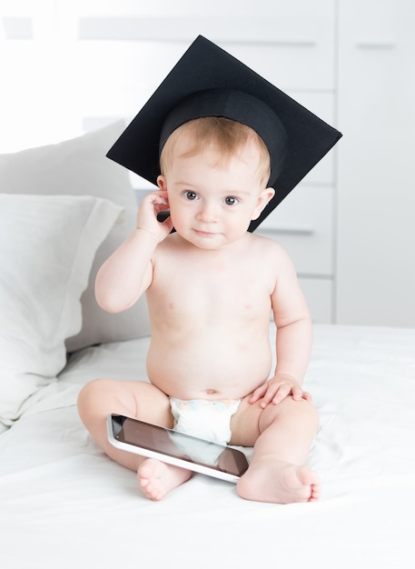 Smart baby boy in graduation cap using digital tablet