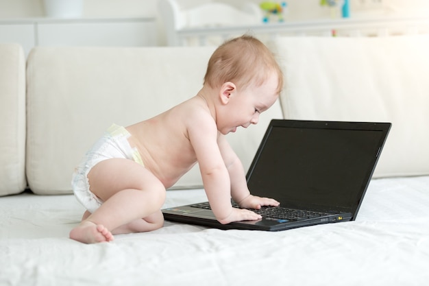 Smart baby in diapers sitting on bed and using laptop