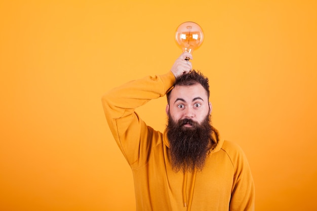 Smart bearded man holding light bulb on his head over yellow background. Creative mind. Bright idea. Succesful man.