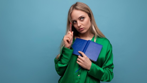 Studente biondo intelligente della giovane donna che medita con il blocco note su fondo blu