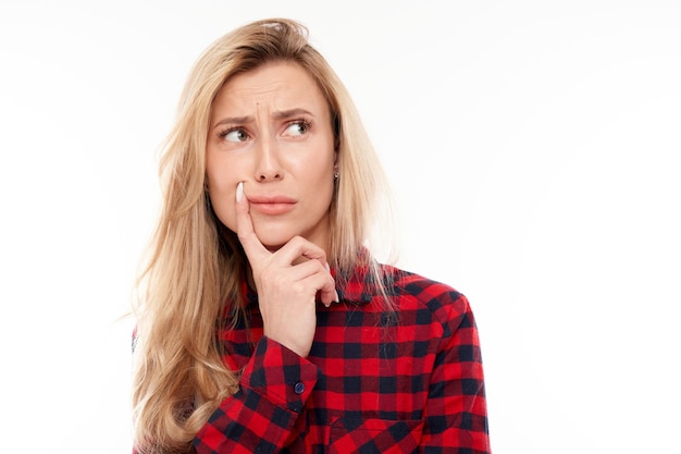 Smart blonde girl in casual holding chin thinks doubts makes decision isolated on white studio background