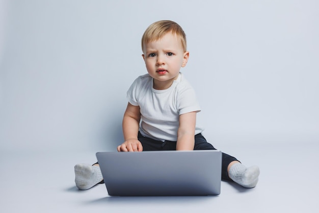 A smart boy 34 years old sits with a laptop on a white\
background a child in a white tshirt and black trousers sits at a\
laptop and looks at the camera modern children