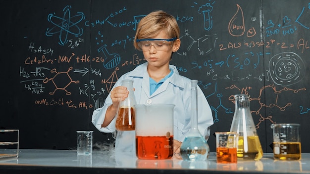 Умный мальчик проверяет смешанную жидкость в лабораторных чашках, держа в руках Эрудицию