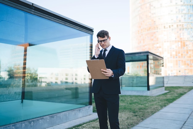 Smart businessman with clipboard speaking on phone