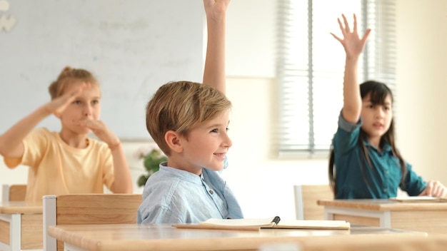 smart caucasian boy raising hand for asking teacher at classroom pedagogy