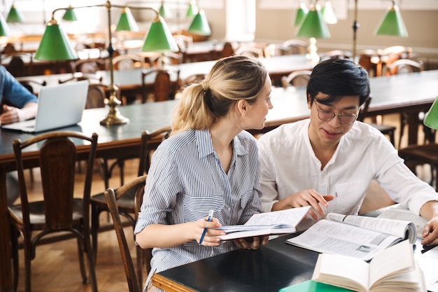 Smart cheerful teenagers studying at the library together, reading books