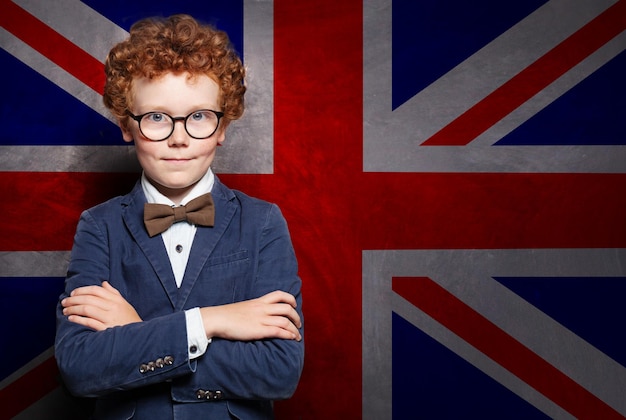 Foto bambino intelligente in abito e occhiali sullo sfondo della bandiera del regno unito concetto di scuola di lingua inglese