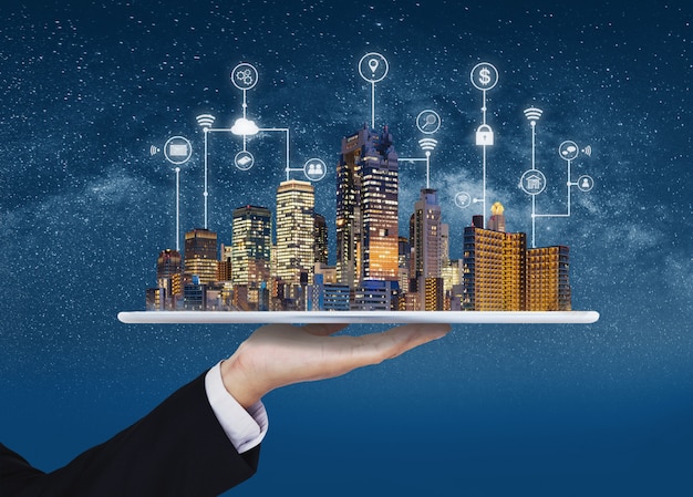 Smart city, tecnologia edile e business immobiliare. uomo d'affari che tiene compressa digitale con l'ologramma delle costruzioni e la tecnologia dell'interfaccia di programmazione dell'applicazione