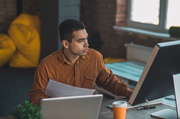 Smart concentrated man holding papers while working in the office