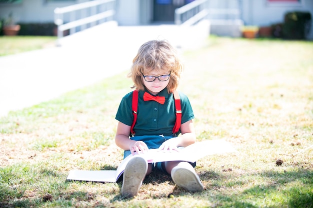 Smart curious nerd in glasses reading book study with copybook outdoor, school education.