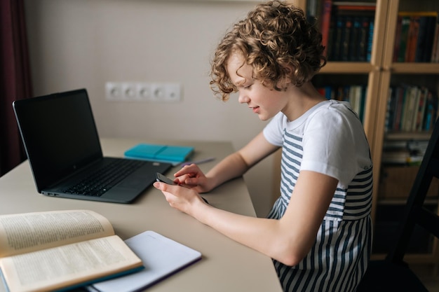 노트북과 스마트폰을 사용하여 집에서 온라인으로 시험 과외를 준비하는 숙제 프로젝트를 원격으로 수행하는 똑똑한 곱슬머리 초반 여학생 학생