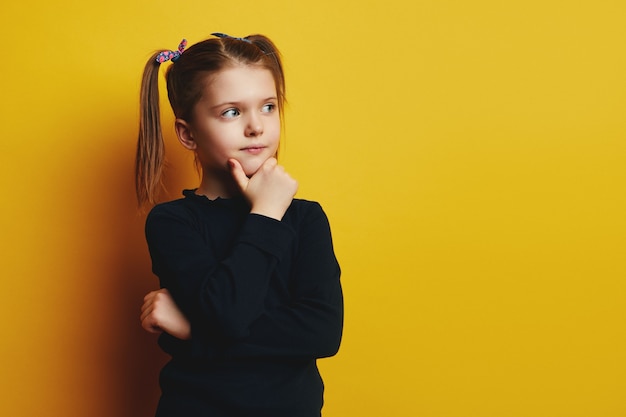 Smart cute adorable kid girl touching cheek and looking up while thinking