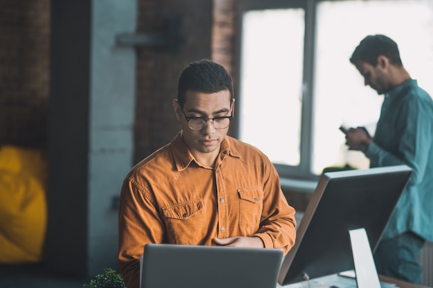 Foto uomo intelligente e diligente concentrandosi sul suo lavoro mentre era seduto davanti ai suoi computer