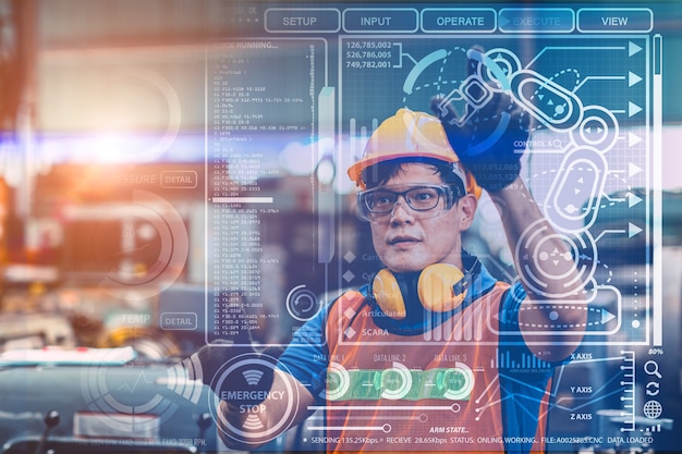 Smart engineer worker using advance technology visual holographic air screen to program and control robotic arm for automated production in modern future factory.