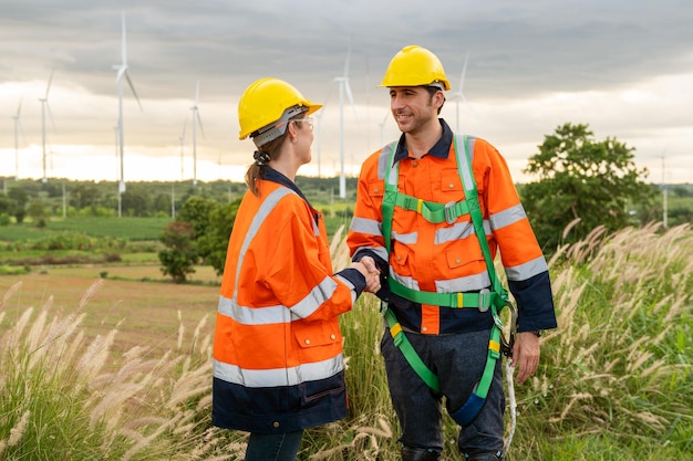 Smart engineers with protective helmet shaking hands at electrical turbines field