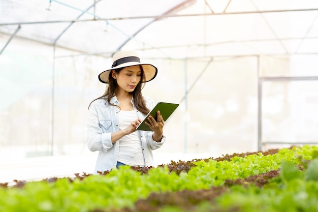 スマートファームとファームテクノロジーのコンセプト。タブレットを使用して温室の有機養液栽培菜園の質と量をチェックするスマートな若いアジアの農家。