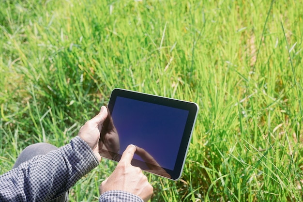 Smart farmer uses a tablet to monitor and analyze the crops in his farm during a sunny day.