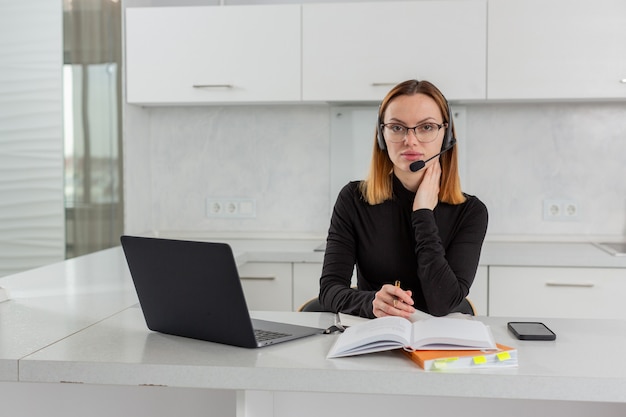 Smart girl in glasses and a headset sits at a laptop in the home office conducts online training high quality photo