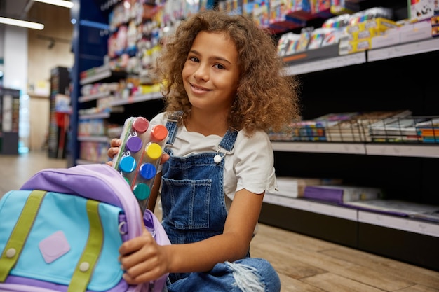 Smart girl putting paints kit into schoolbag