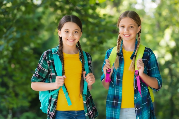똑똑한 소녀들의 어린 시절 행복 학교 교복을 입은 두 자매는 야외에서 휴가를 보낼 준비가 되어 있습니다. 행복한 십대 아이들은 봄에 걷는 작은 여학생들에게 배낭을 메고 돌아갑니다.