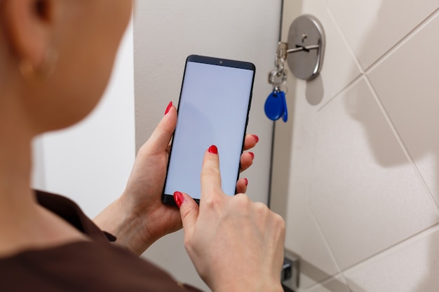 smart house, home automation, device with app icons. Woman uses smartphone with smarthome security app to unlock the door of house.