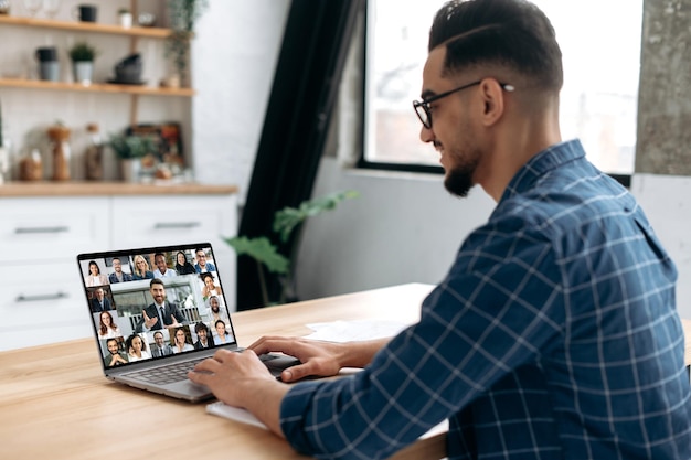 Smart indian or arabian guy meet with a group of multiracial\
colleagues gathered in a video conference to communicate and\
discuss work issues and new project planning business plan group\
brainstorm