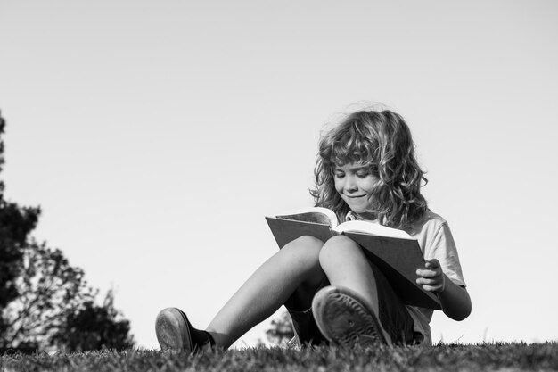 屋外の公園で本を読んでスマートな子供の男の子