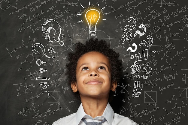 Photo smart kid with lightbulb brainstorming and idea concept little cute student boy on chalkboard background