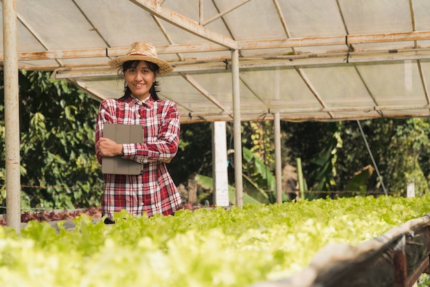 Smart landbouwer en plantaardige producten concept; vrouwelijke tuinman die vers installaties in landbouwbedrijf met tablet controleren en toepassing gebruiken voor steun slim landbouwbedrijf