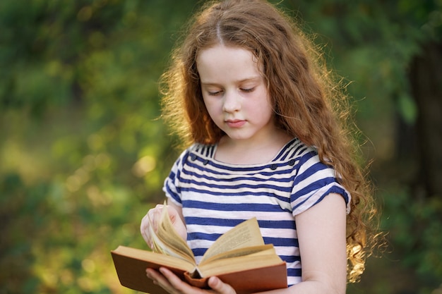 야외에서 책을 읽고 스마트 작은 소녀.