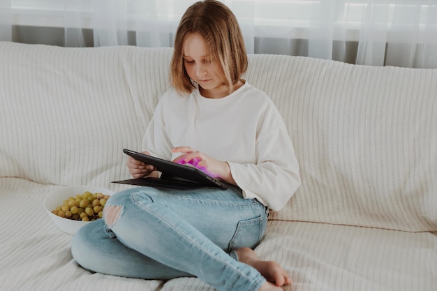 Smart little girl using tablet computer while sitting on couch in living room at home