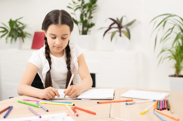 Scolara intelligente con penna e libri che scrivono un test in un'aula. bambino in una scuola elementare. educazione e apprendimento per i bambini.