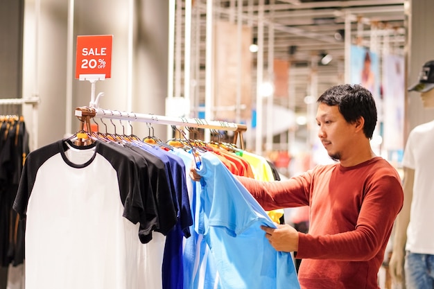 Uomo astuto con la barba che sceglie i vestiti nel negozio di vestiti al centro commerciale