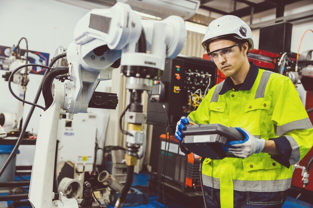 Foto ingegnere moderno intelligente maschio che utilizza la moderna tecnologia robot impostazione del braccio di saldatura robotico nel processo di produzione automatizzata in fabbrica