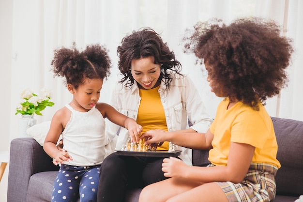 Smart mother good care, teaching her childs to be genius and clever little girls learning to play chess boardgame in holiday at home.