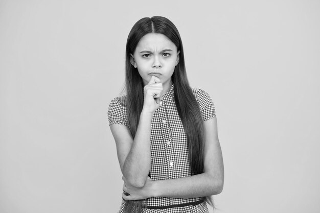 Smart nerdy school girl touching cheek and thinking against yellow background Child think and idea concept Thinking pensive clever teenager girl