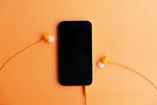 Photo smart phone and earphone on orange background